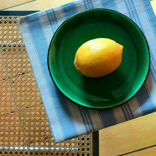Un citron jaune dans une assiette verte et serviette de table en tissu kelsch rayée bleu et écru