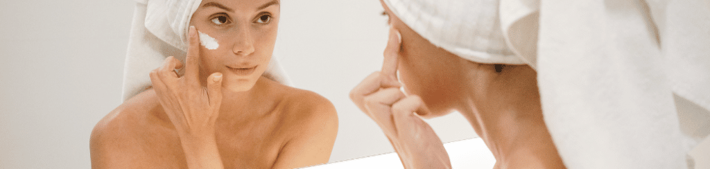 Femme dans le miroir qui s'applique de la crème sur le visage