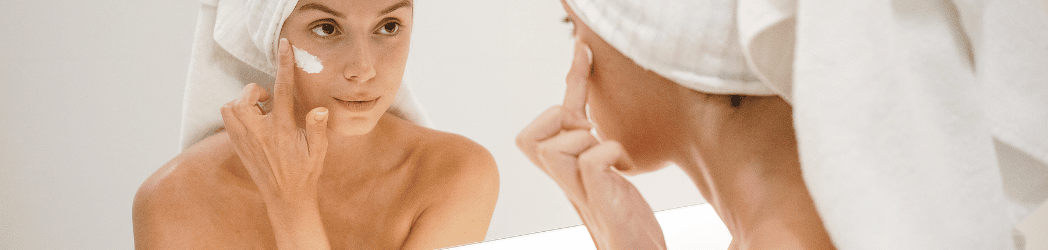 Femme dans le miroir qui s'applique de la crème sur le visage